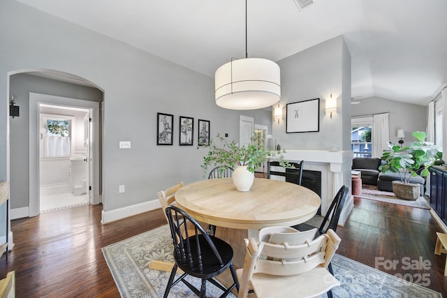 dining area featuring arched walkways, vaulted ceiling, dark wood-style floors, baseboards, and a fireplace
