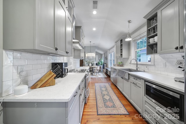kitchen featuring a sink, open shelves, stainless steel appliances, backsplash, and gray cabinetry