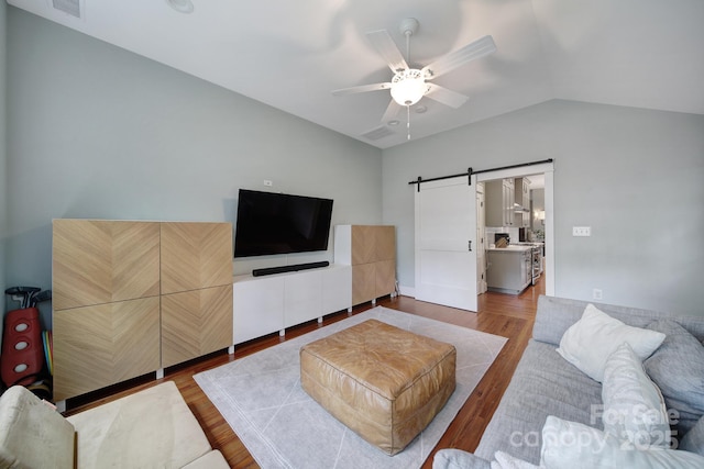 living room featuring a barn door, vaulted ceiling, wood finished floors, and a ceiling fan