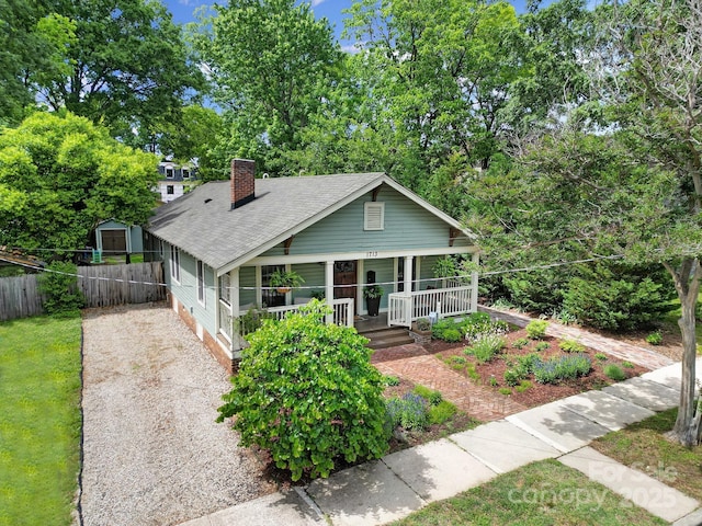bungalow-style house with a porch, fence, a chimney, roof with shingles, and a storage unit