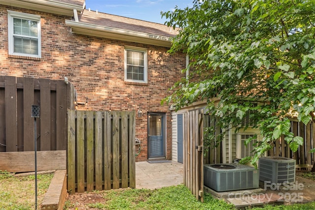 rear view of property with central air condition unit, brick siding, and fence