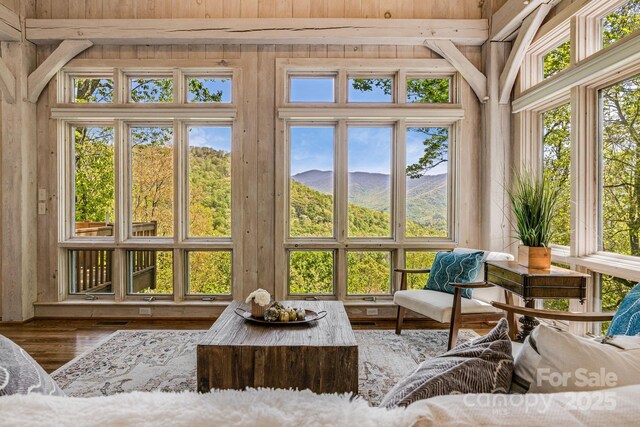 sunroom with wood finished floors, a mountain view, healthy amount of natural light, and wood walls