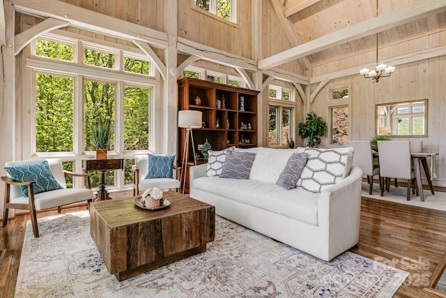 living area with high vaulted ceiling, a chandelier, wooden walls, plenty of natural light, and wood finished floors