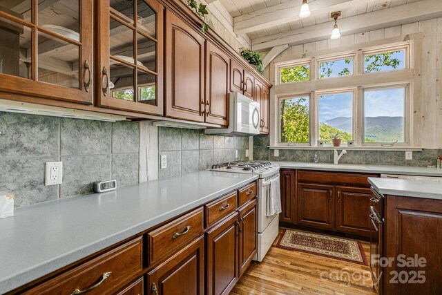 kitchen with white appliances, a sink, light wood-style flooring, backsplash, and wood ceiling