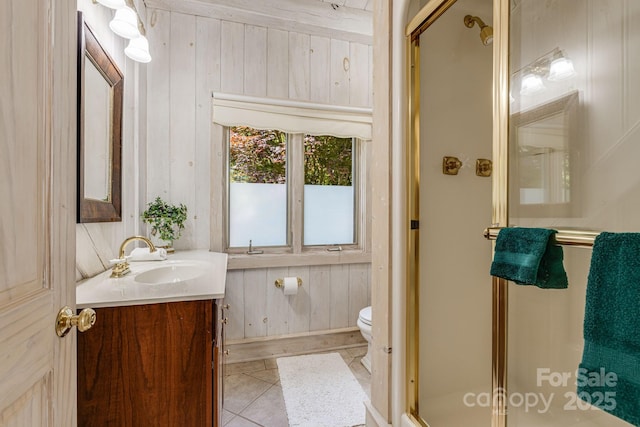 bathroom with a stall shower, wood walls, toilet, vanity, and tile patterned flooring
