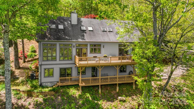 back of property with a chimney, a wooden deck, and roof with shingles