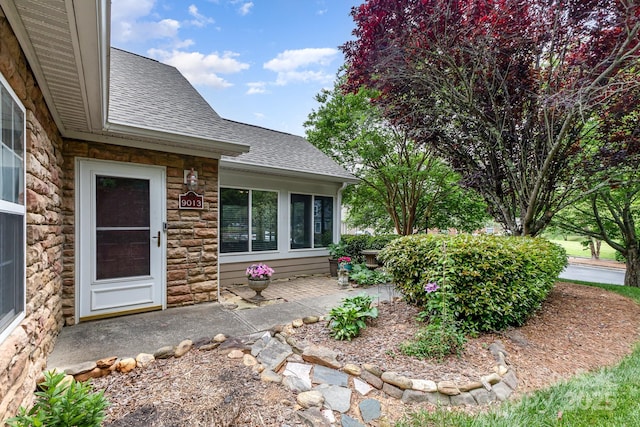 doorway to property featuring stone siding and a shingled roof