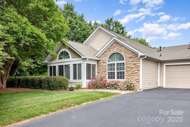 ranch-style home featuring driveway, a front yard, an attached garage, stone siding, and roof with shingles