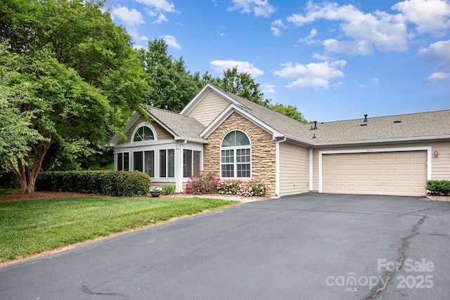 view of front facade featuring driveway, a front yard, a garage, stone siding, and roof with shingles