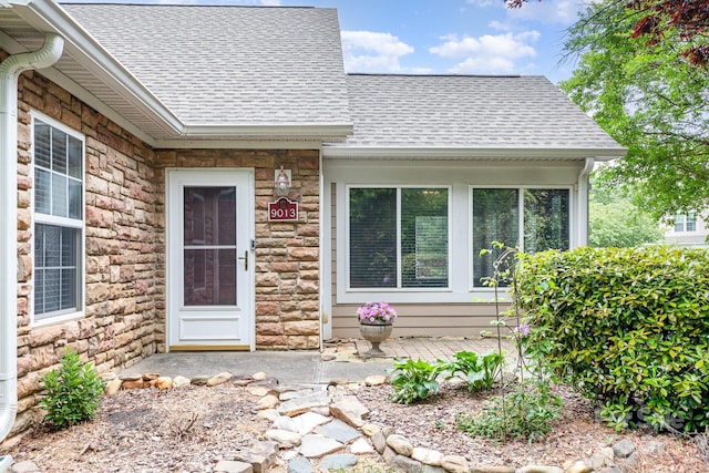 entrance to property featuring a shingled roof and stone siding