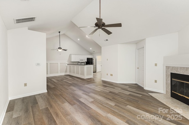 unfurnished living room with lofted ceiling, wood finished floors, visible vents, ceiling fan, and a tile fireplace
