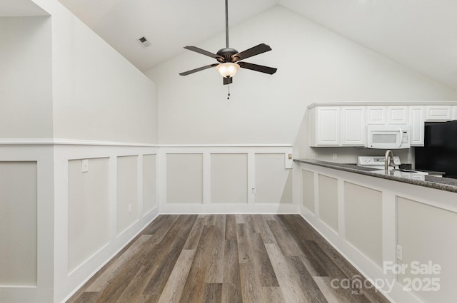 unfurnished dining area with a ceiling fan, dark wood-style flooring, a sink, a decorative wall, and high vaulted ceiling