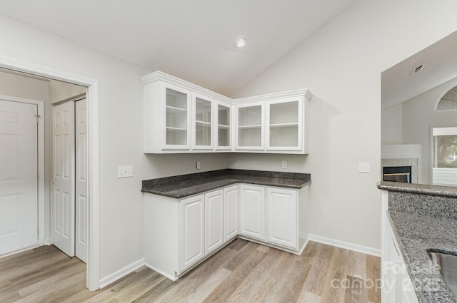 kitchen featuring lofted ceiling, dark stone counters, light wood-style flooring, white cabinetry, and glass insert cabinets