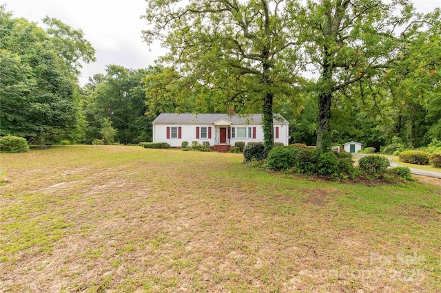 view of front of property featuring a front yard, an outdoor structure, a storage shed, and a forest view