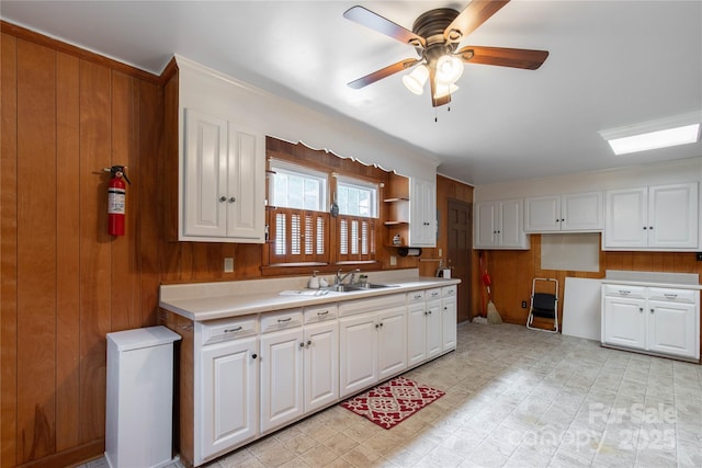 kitchen with a sink, wood walls, ceiling fan, white cabinets, and light countertops