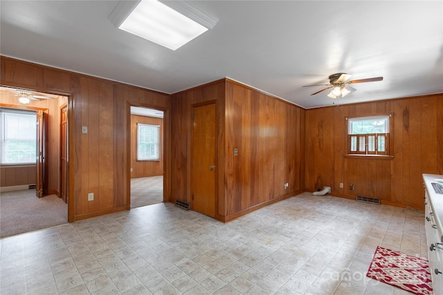 unfurnished room with ceiling fan, healthy amount of natural light, wooden walls, light floors, and baseboards