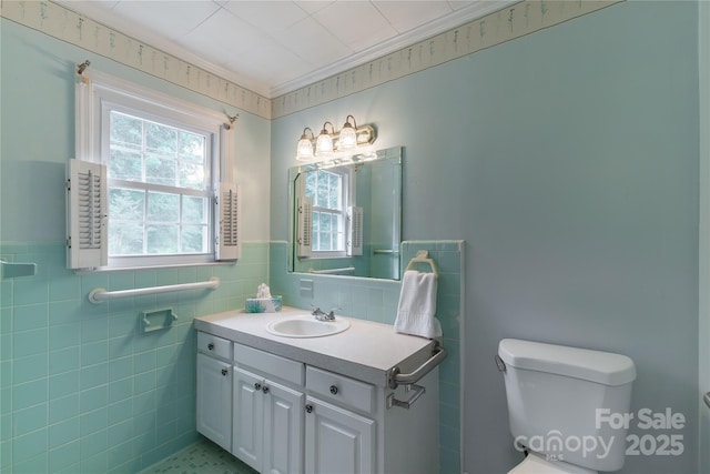 bathroom featuring toilet, vanity, wainscoting, and tile walls