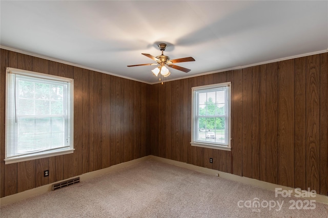 carpeted empty room with a ceiling fan and wood walls