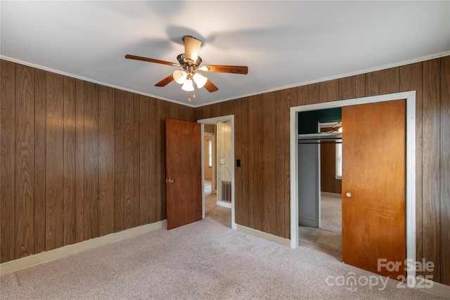 unfurnished bedroom with carpet flooring, a closet, a ceiling fan, ornamental molding, and wood walls