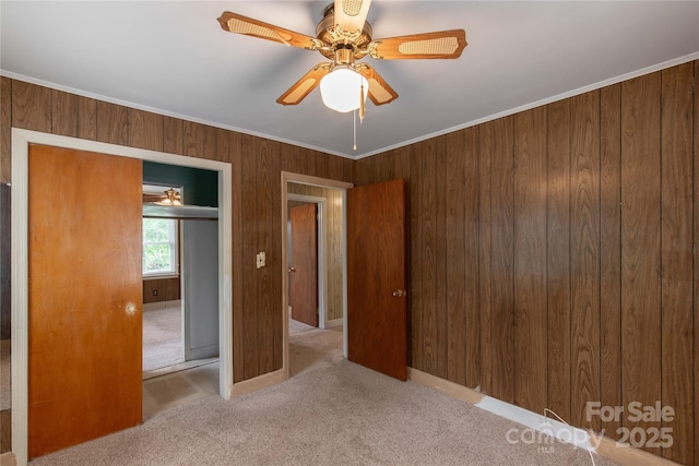 unfurnished bedroom with carpet floors, wood walls, ornamental molding, a ceiling fan, and a closet