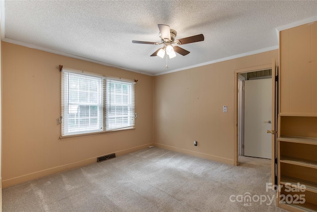 carpeted empty room with a ceiling fan, ornamental molding, a textured ceiling, and baseboards