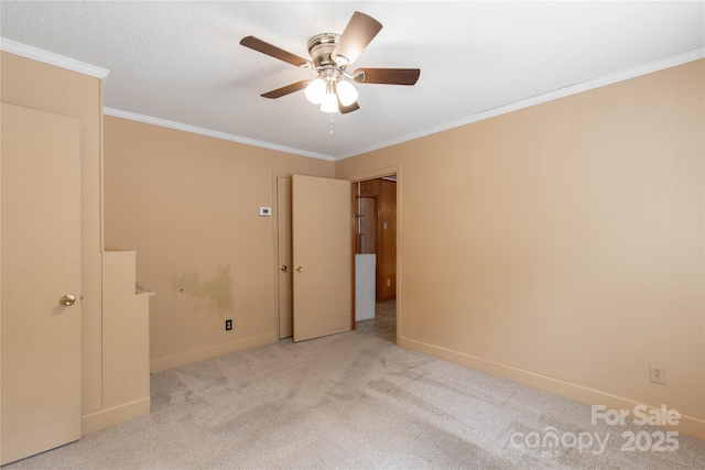 carpeted spare room featuring a ceiling fan, ornamental molding, and baseboards