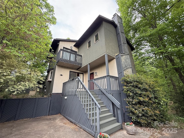 rear view of house featuring stairs, a chimney, fence, and a balcony