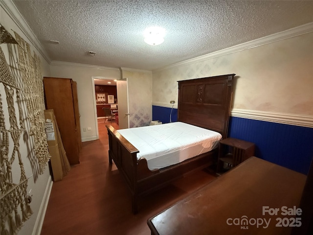 bedroom with wainscoting, crown molding, a textured ceiling, and wood finished floors