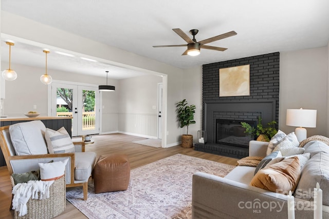 606 Hillcrest St, Hudson, NC 28638 - living area featuring a wainscoted wall, french doors, a fireplace, a ceiling fan, and light wood-style floors