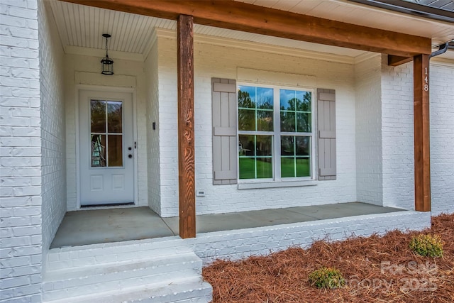 entrance to property featuring a porch and brick siding