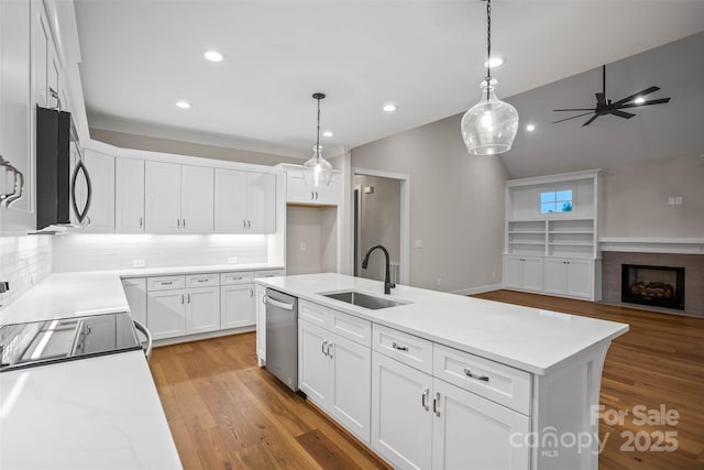 kitchen featuring a sink, open floor plan, white cabinetry, backsplash, and appliances with stainless steel finishes