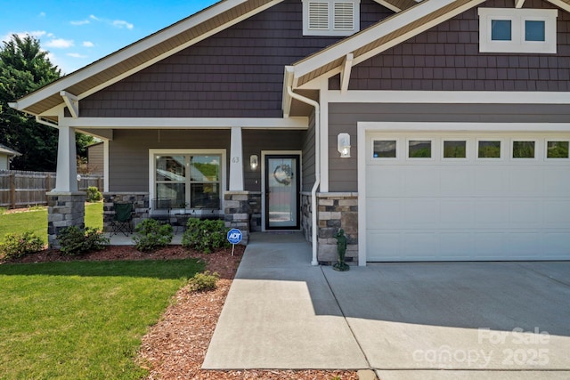 craftsman house featuring covered porch, stone siding, fence, a front lawn, and driveway