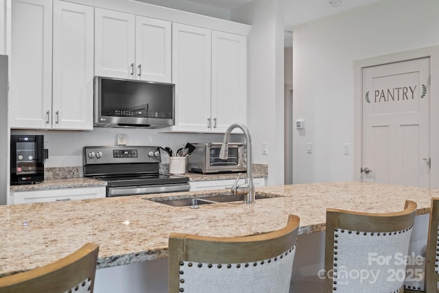 kitchen with light stone countertops, a breakfast bar area, a sink, white cabinetry, and stainless steel appliances