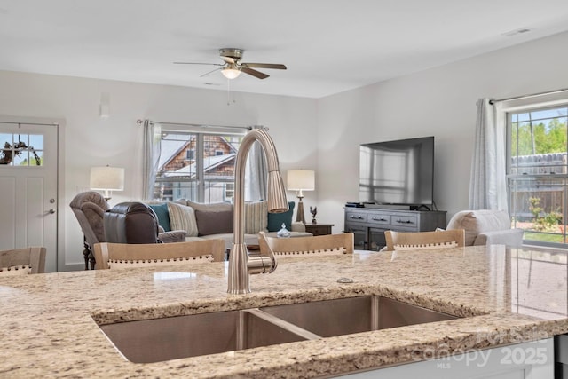 kitchen featuring a ceiling fan, light stone counters, visible vents, a sink, and open floor plan