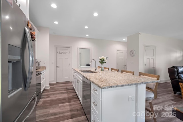kitchen featuring a sink, a breakfast bar, dark wood-style flooring, white cabinetry, and appliances with stainless steel finishes