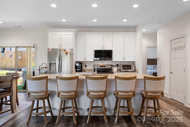 kitchen featuring white cabinets, appliances with stainless steel finishes, light stone countertops, and an island with sink