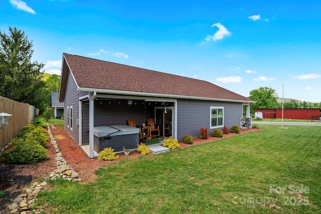 rear view of property with a yard, roof with shingles, a hot tub, and fence
