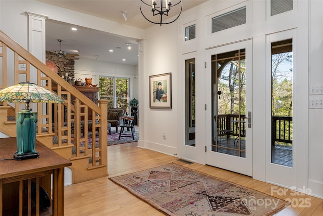 foyer with ceiling fan with notable chandelier, ornate columns, visible vents, stairway, and light wood-style floors