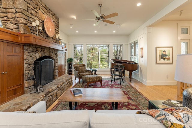 living room with a ceiling fan, light wood-style flooring, recessed lighting, baseboards, and a stone fireplace