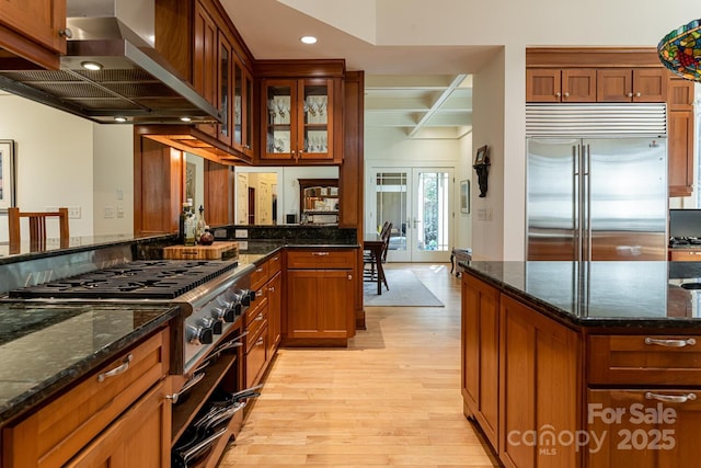 kitchen featuring exhaust hood, light wood finished floors, beamed ceiling, stove, and built in refrigerator