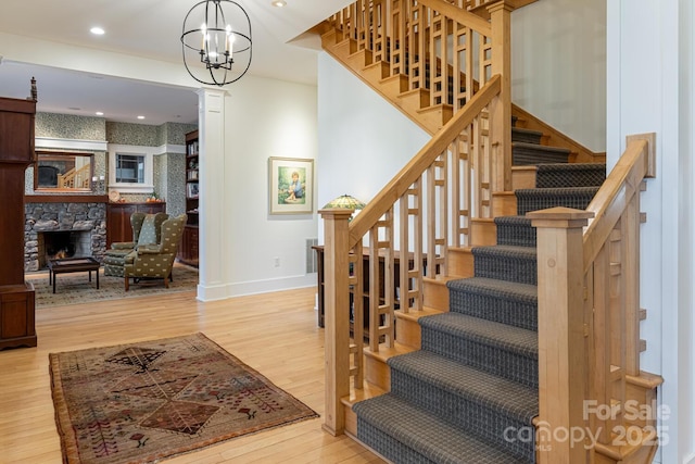 staircase with wood finished floors, recessed lighting, a notable chandelier, baseboards, and a stone fireplace