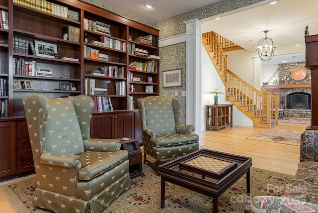 living area featuring stairs, wood finished floors, a fireplace, a notable chandelier, and wallpapered walls