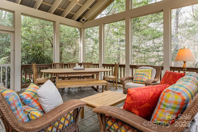 sunroom with an outdoor living space, stone finish flooring, outdoor dining area, and high vaulted ceiling