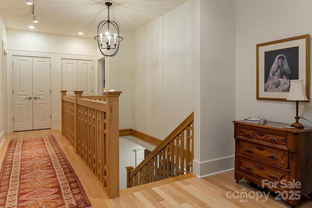 hallway featuring light wood-style floors, a chandelier, an upstairs landing, and baseboards