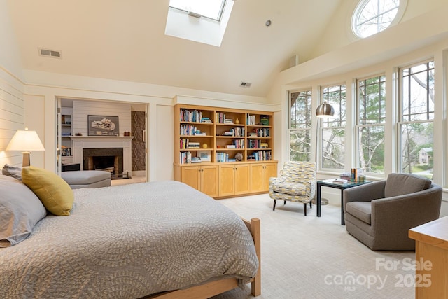 bedroom featuring a fireplace with raised hearth, visible vents, high vaulted ceiling, light carpet, and a skylight