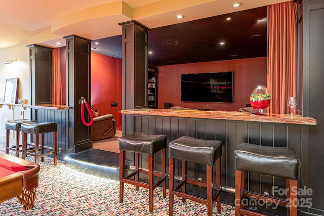 bar with a bar, ornate columns, carpet, and recessed lighting