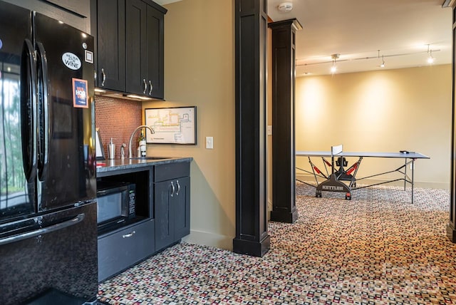 kitchen with baseboards, a sink, backsplash, black appliances, and dark stone counters