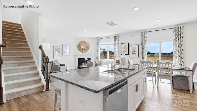 kitchen with a sink, dark stone counters, visible vents, dishwasher, and light wood-style floors