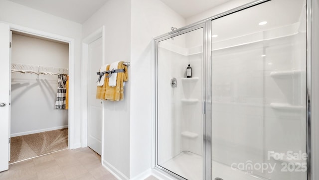 bathroom with a stall shower, a walk in closet, baseboards, and tile patterned floors
