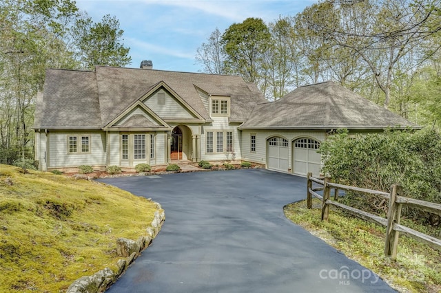 shingle-style home featuring asphalt driveway, an attached garage, a shingled roof, and a chimney